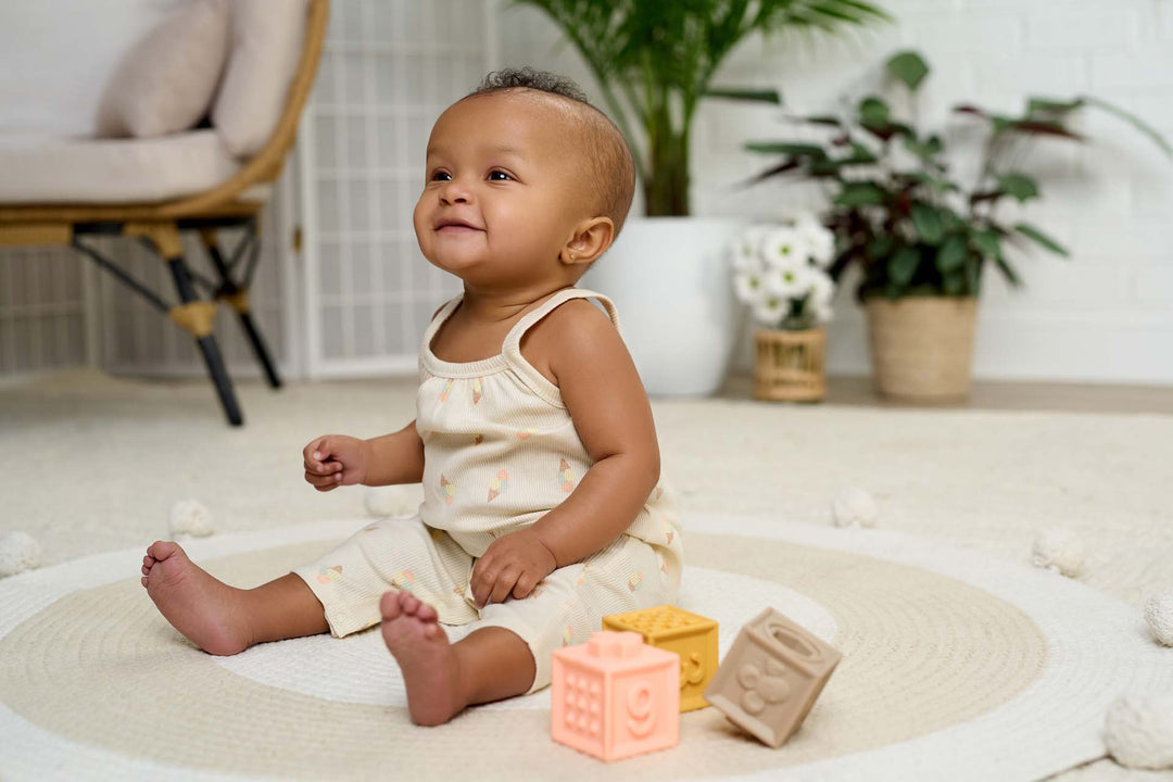 Smiling baby girl wearing a romper playing with blocks.