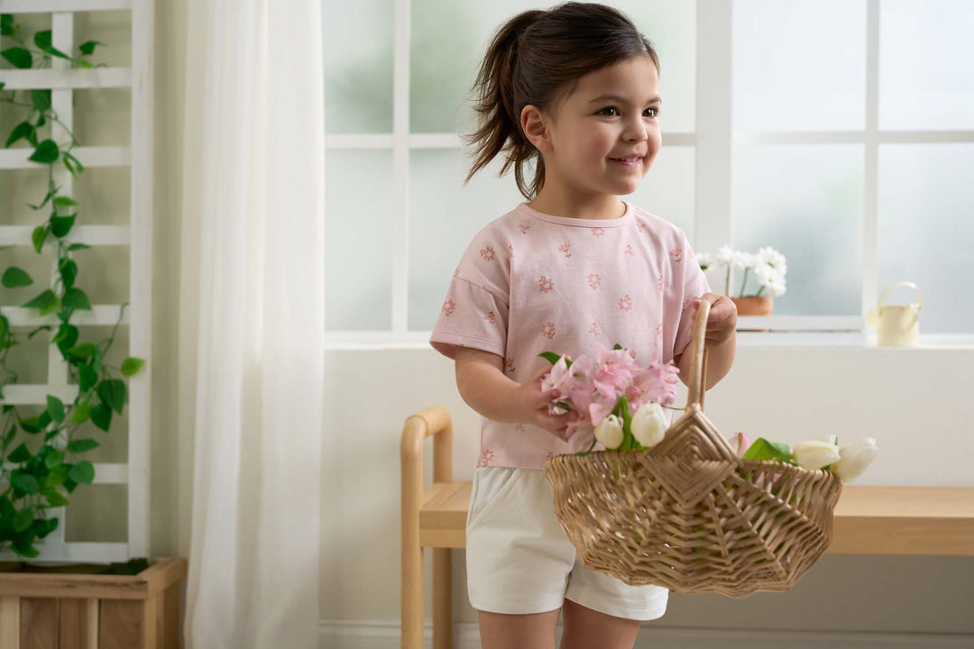 A cute toddler girl wearing a pink shirt and holding a basket of flowers.