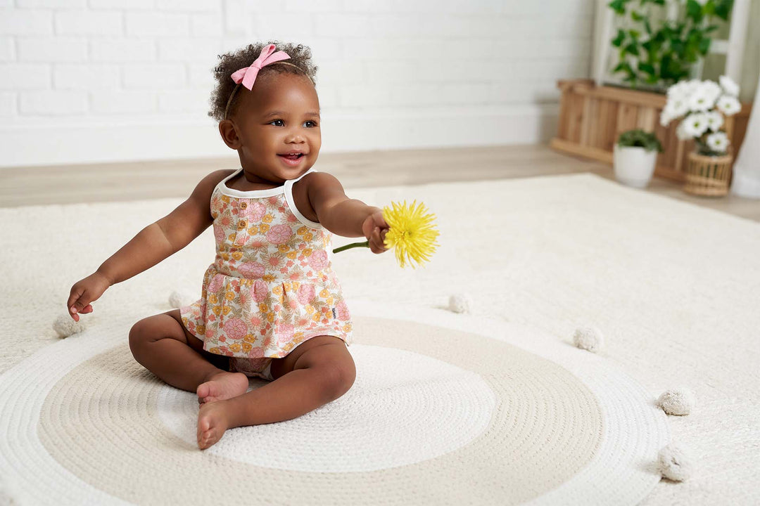 Cute baby girl wearing a floral bodysuit holding a yellow flower.