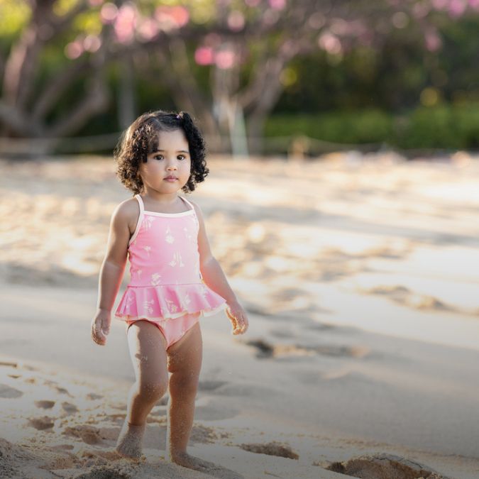 A little girl in a pink bathing suit walking on the beach.