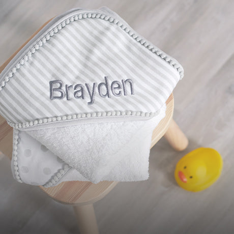 Grey stripped blanket with embroidery with name Brayden laying on a wooden stool.