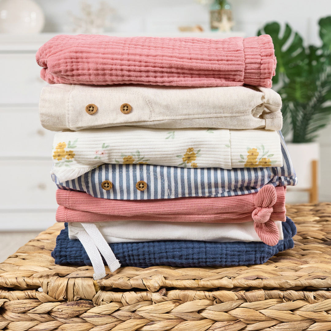 A stack of neatly folded baby and toddler summer shorts, including varied textures and patterns, on a woven basket.