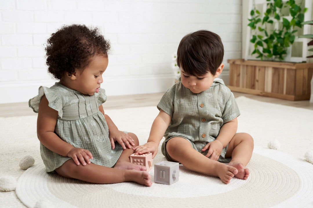 Girl and boy babies wearing green outfits playing with blocks.