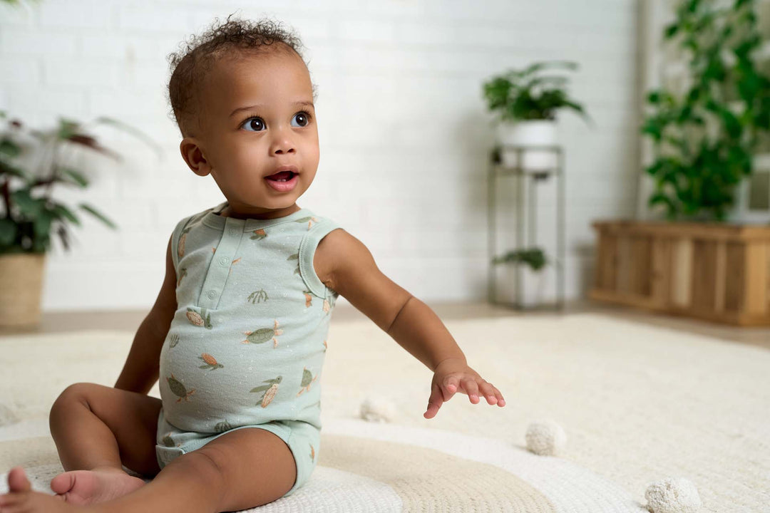 Baby boy wearing a light blue bodysuit with a turtle print.