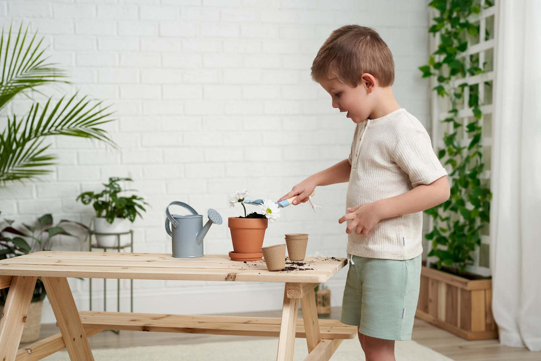 A toddler boy is planting a plant on a wooden table.