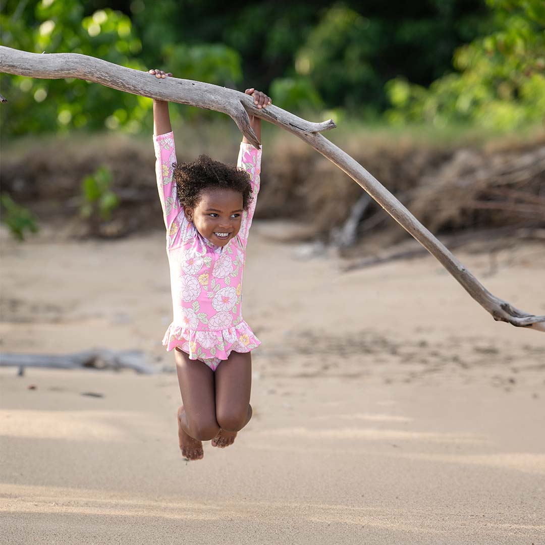 A young girl is hanging from a branch on the beach