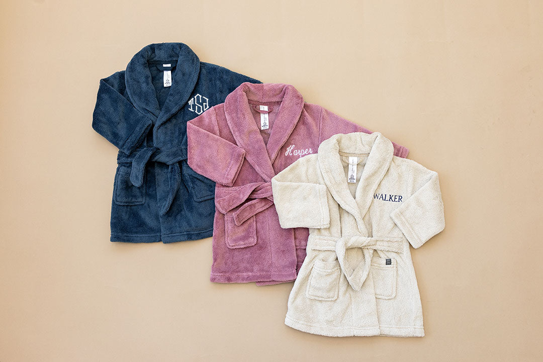 Three bathrobes in blue, pink, and white on a beige background