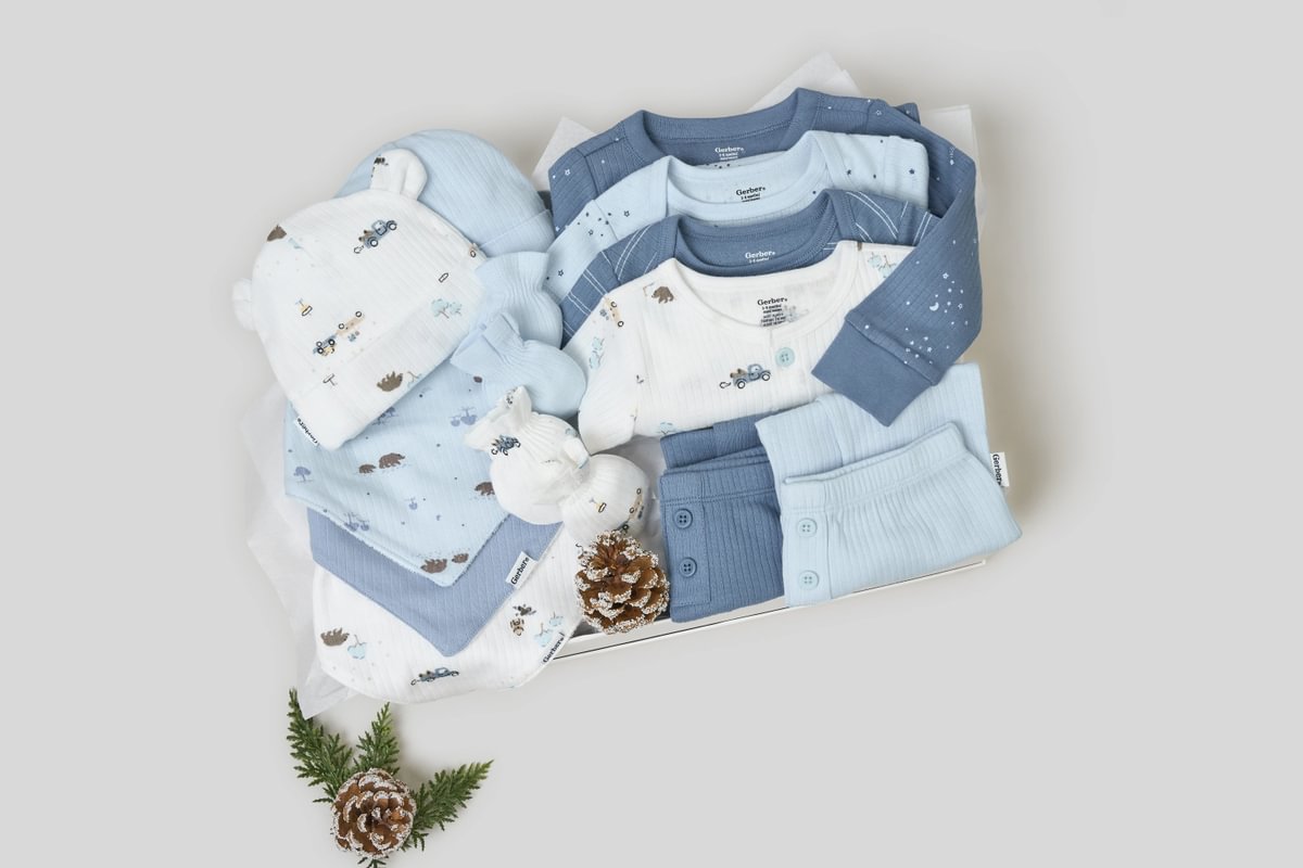 Collection of baby clothes in blue and white on a light gray background with pine cones.