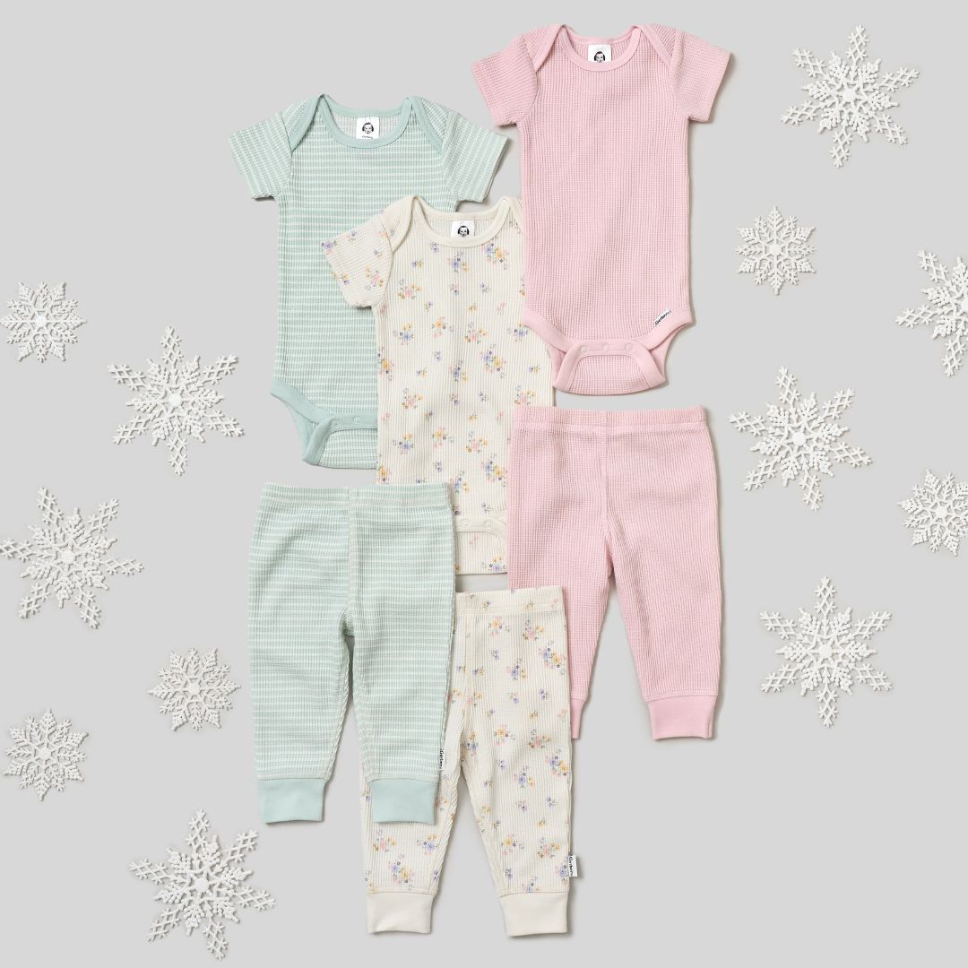 Set of baby clothing including onesies and pants on a light gray background with snowflake decorations.