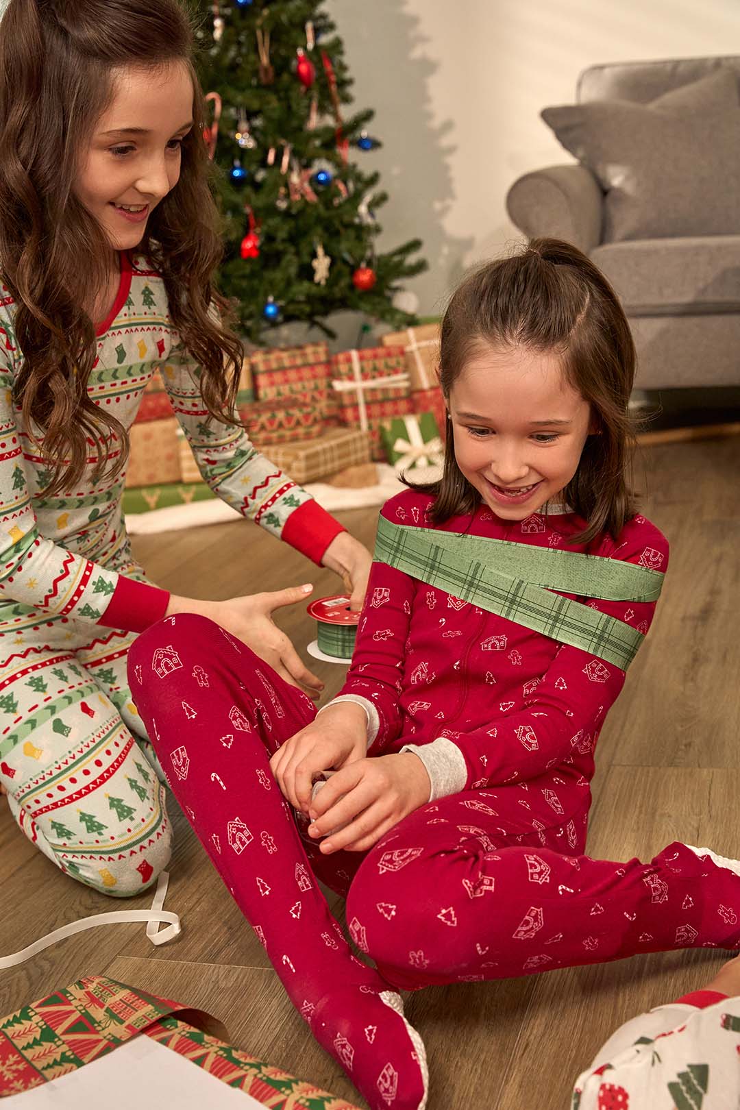 Two children in festive pajamas sitting on the floor near a Christmas tree.