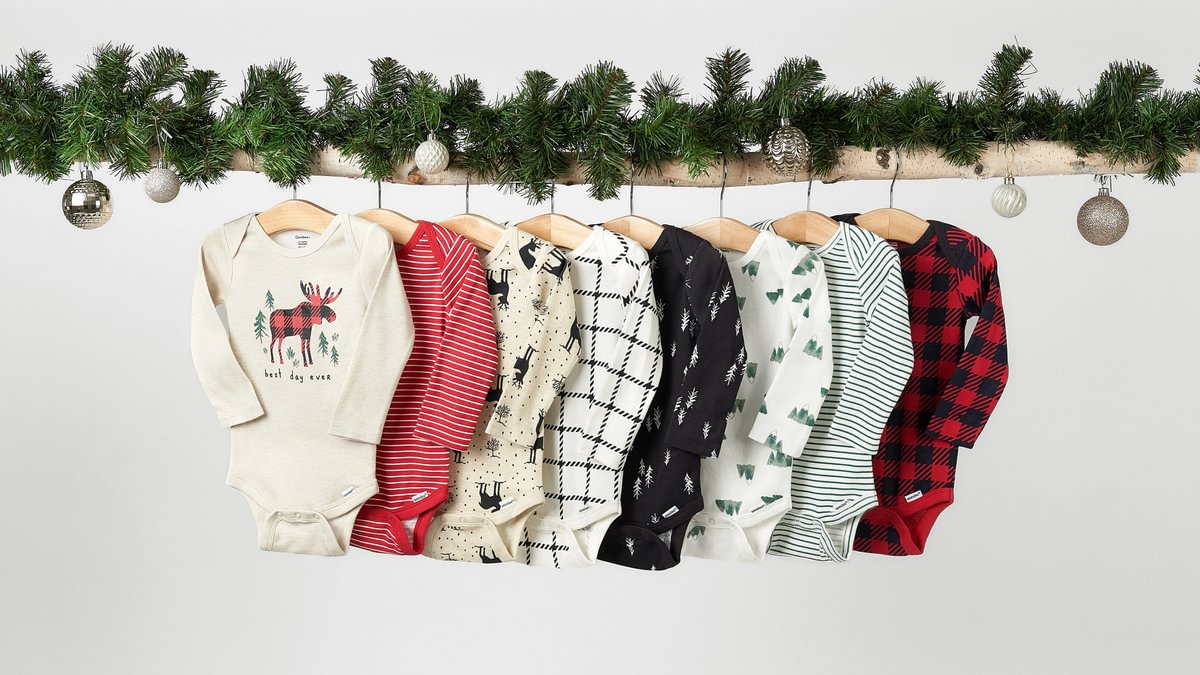 Row of children's Christmas-themed outfits on hangers with a decorative garland above.