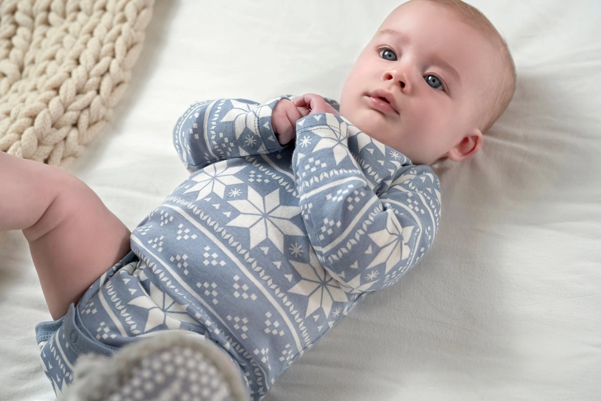 Baby wearing blue and white patterned pants lying on a white surface.