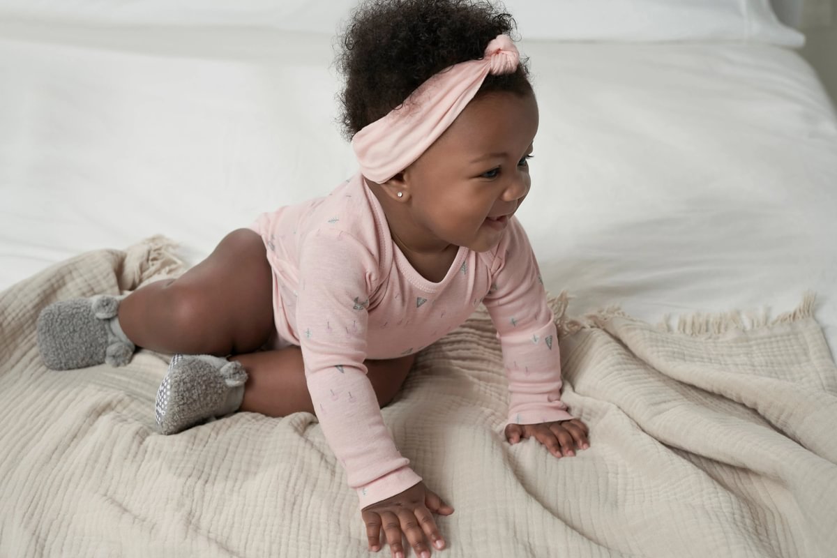 Baby in a pink outfit and headband sitting on a white blanket