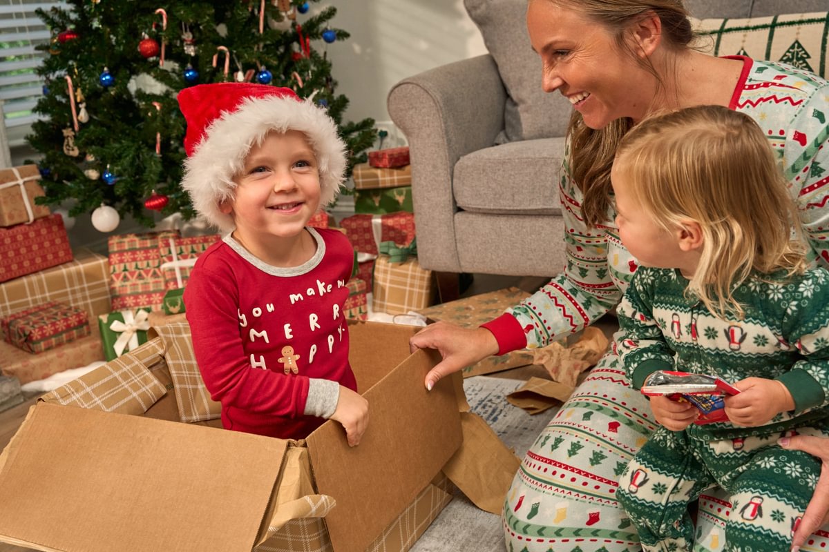 Woman and two children in pajamas with a Christmas tree and presents in the background