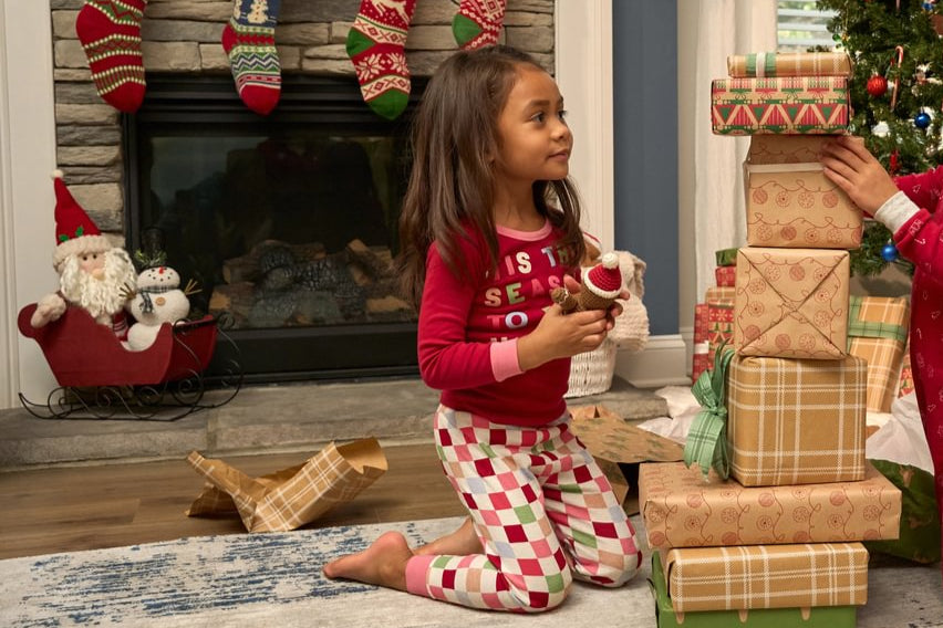 Child in pajamas playing with Christmas presents in a festive living room.