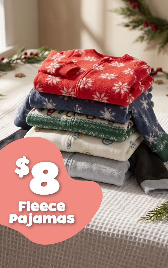 A stack of five folded fleece pajamas in holiday colors sits on a waffle-knit tablecloth with Christmas greenery in the background. A pink price badge in the lower left reads '$8 Fleece Pajamas'.