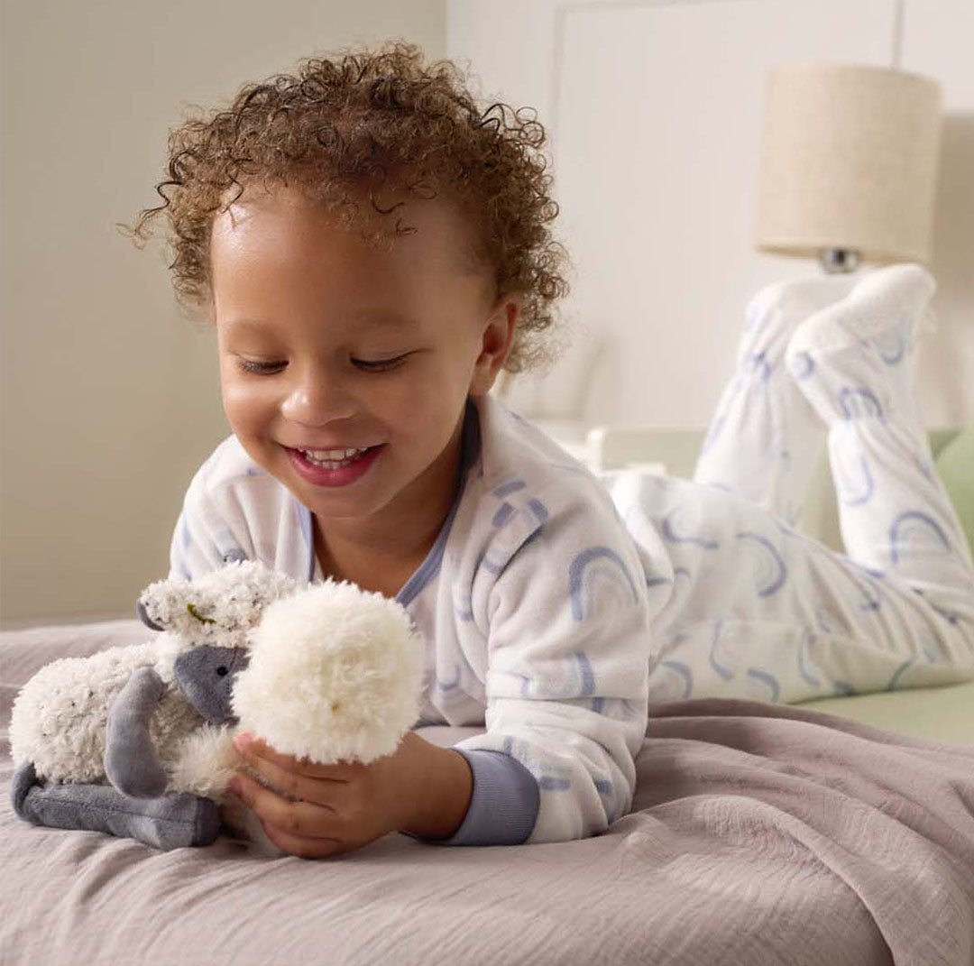 Child in pajamas holding a plush toy on a bed