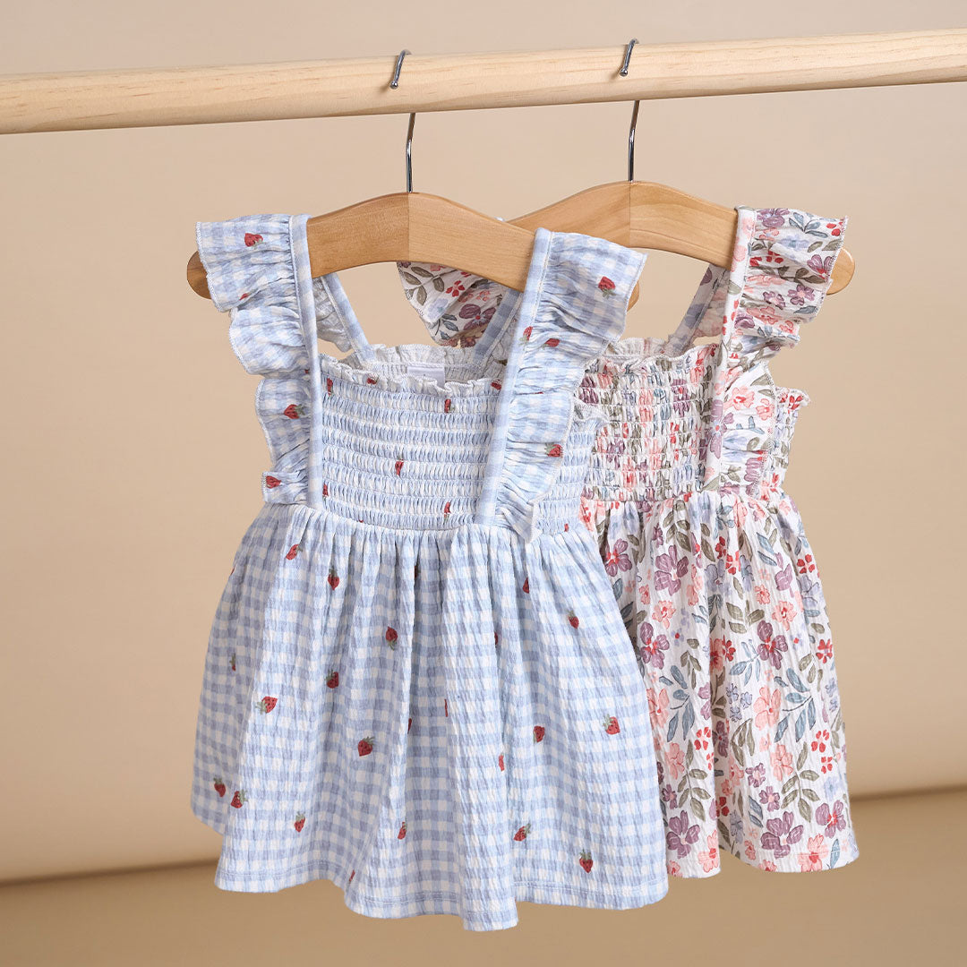 Two children's dresses hanging on a wooden hanger against a beige background