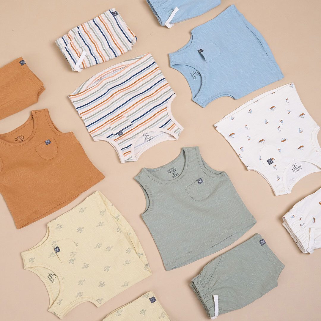 Collection of baby clothes including shirts, shorts, and pants on a beige background