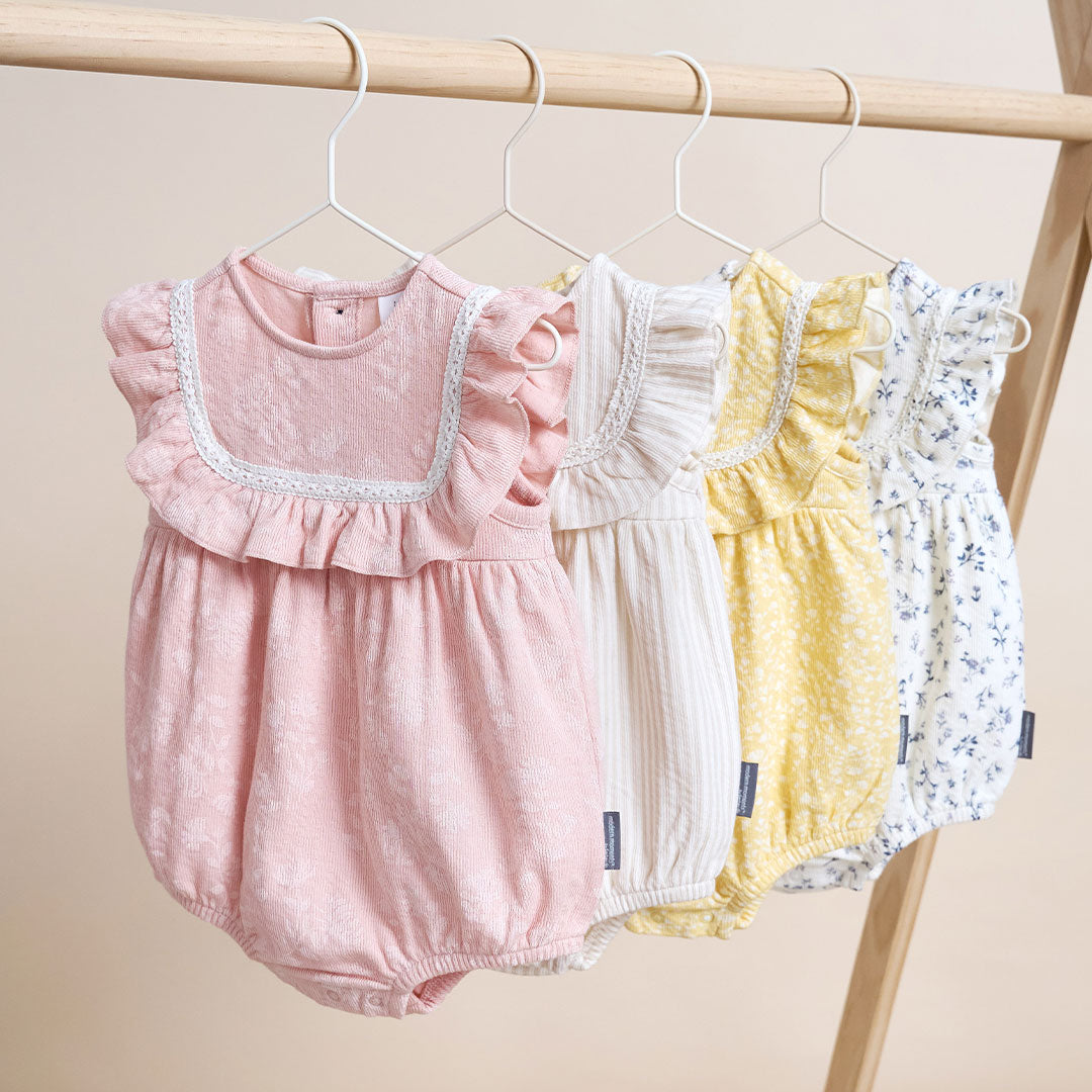 Three baby rompers hanging on a rack against a beige background