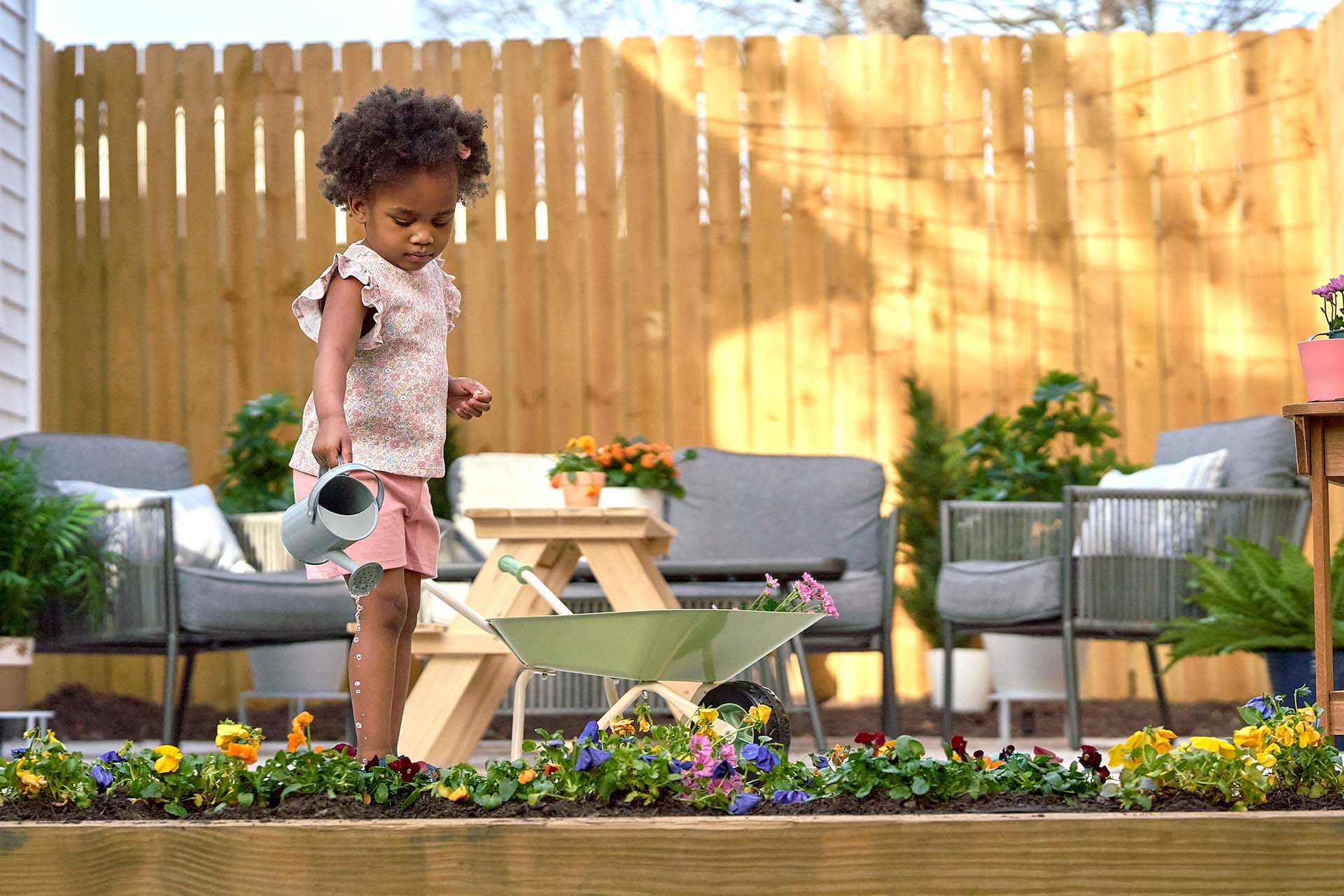 Child with a watering can and wheelbarrow in a garden setting