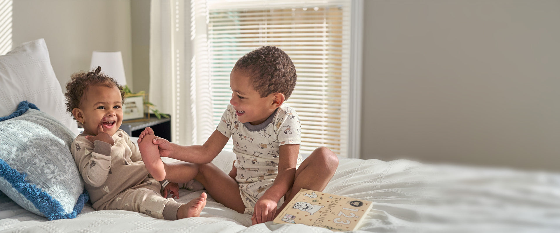 Two children sitting on a bed, laughing and playing with a book.