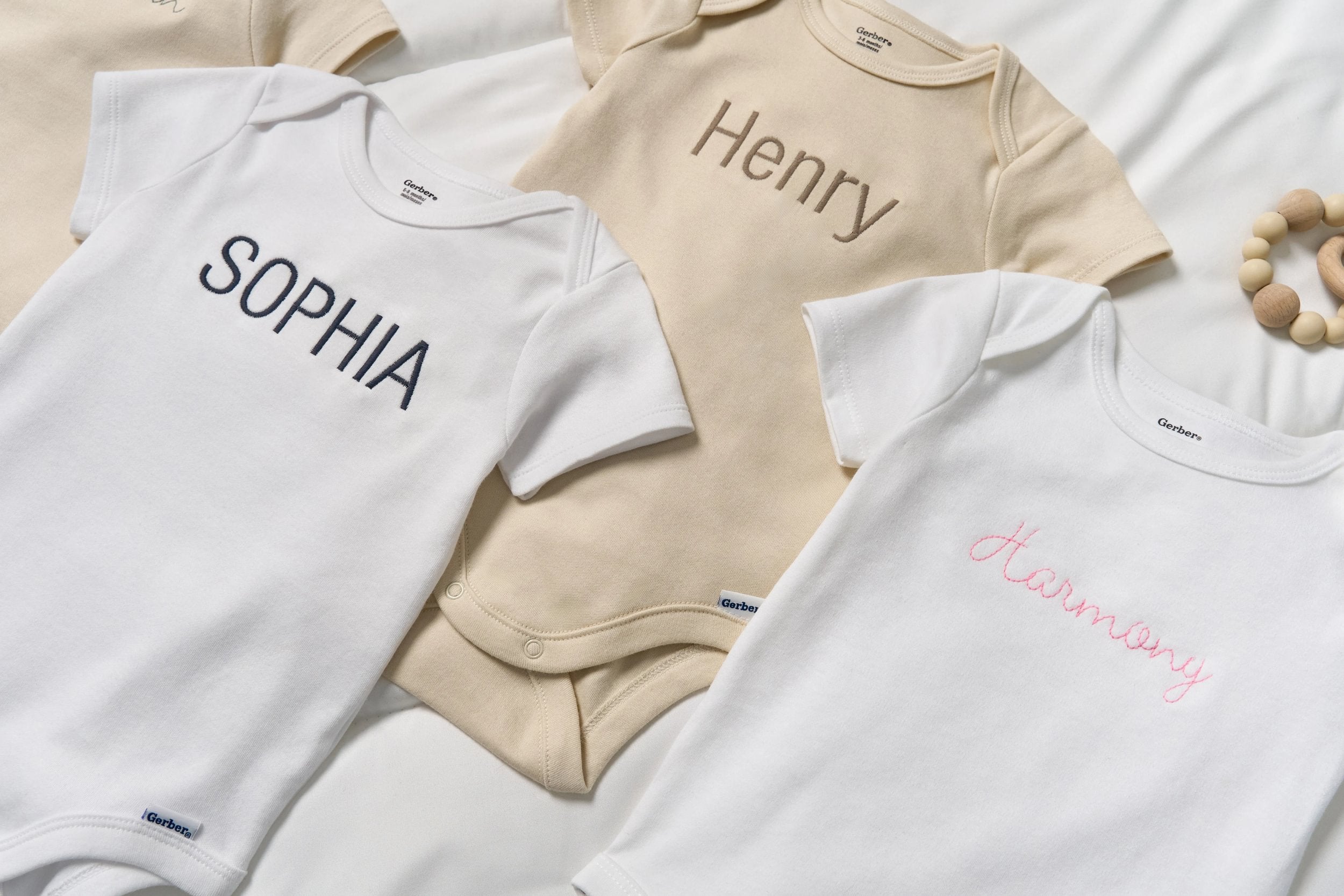 Three baby onesies with embroidered names on a white background