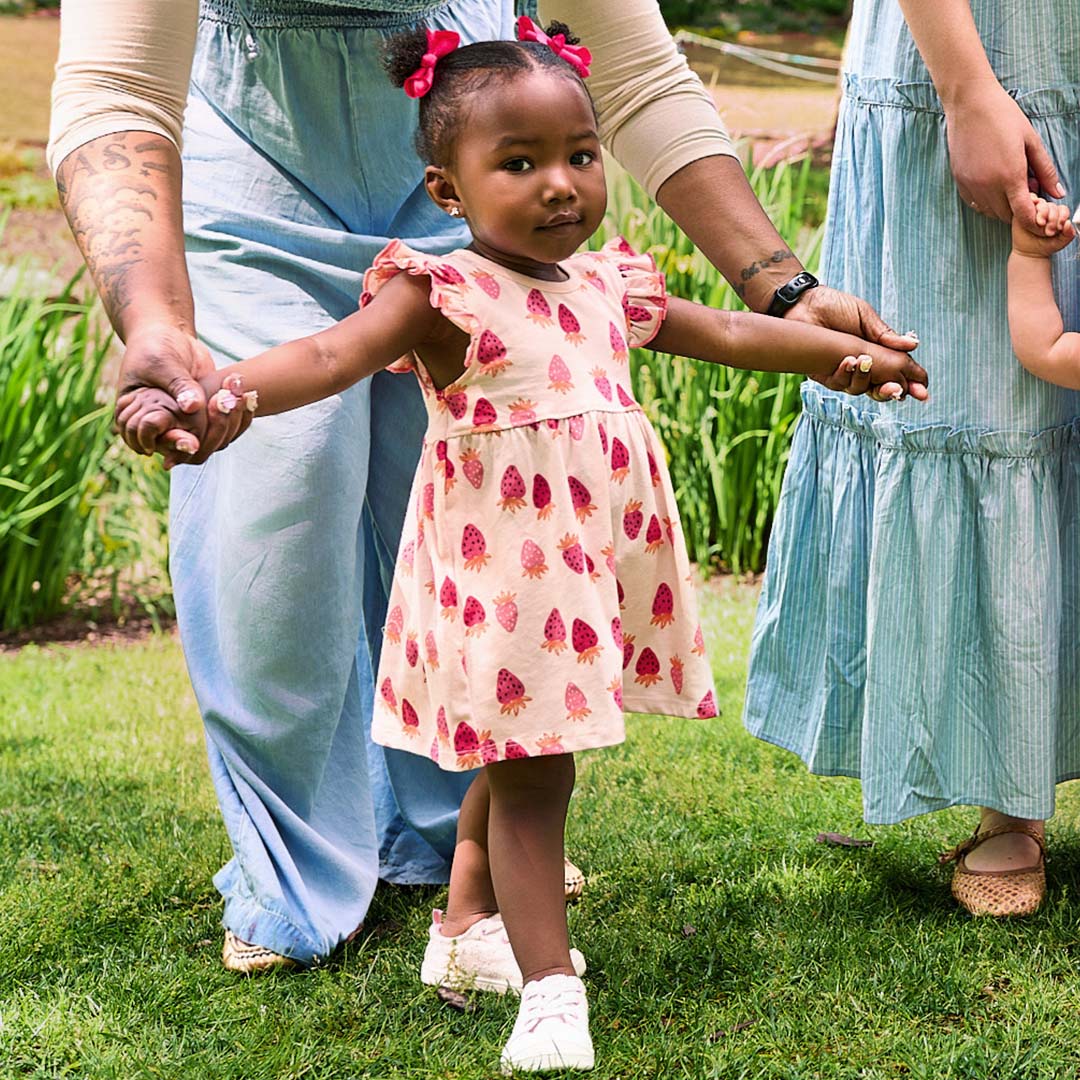 Child in a pink dress with strawberries patterns standing outdoors with adults