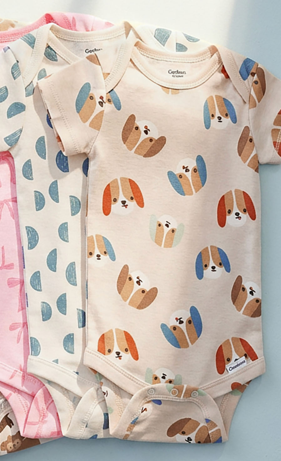 As stack of baby bodysuits with dog pattern on a light blue background