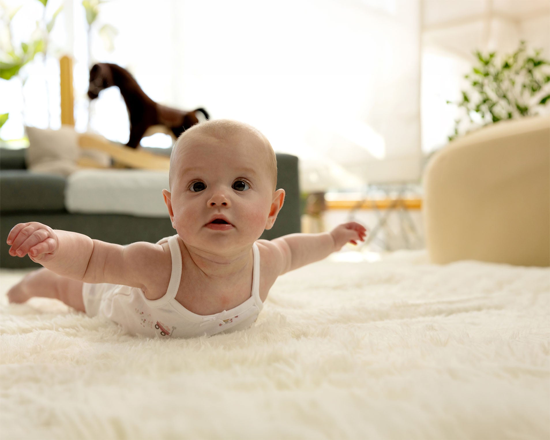 Baby wearinig a white bodysuit lying on a soft surface with a blurred background