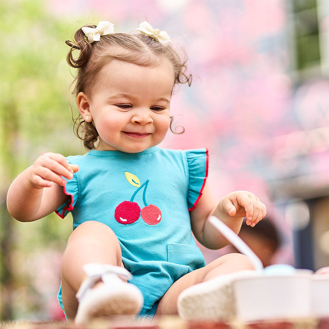 Child in a blue romper with cherry design sitting outdoors