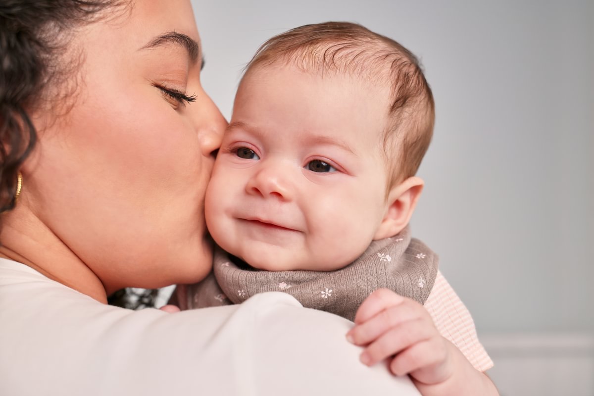Woman kissing a baby on the cheek against a plain background