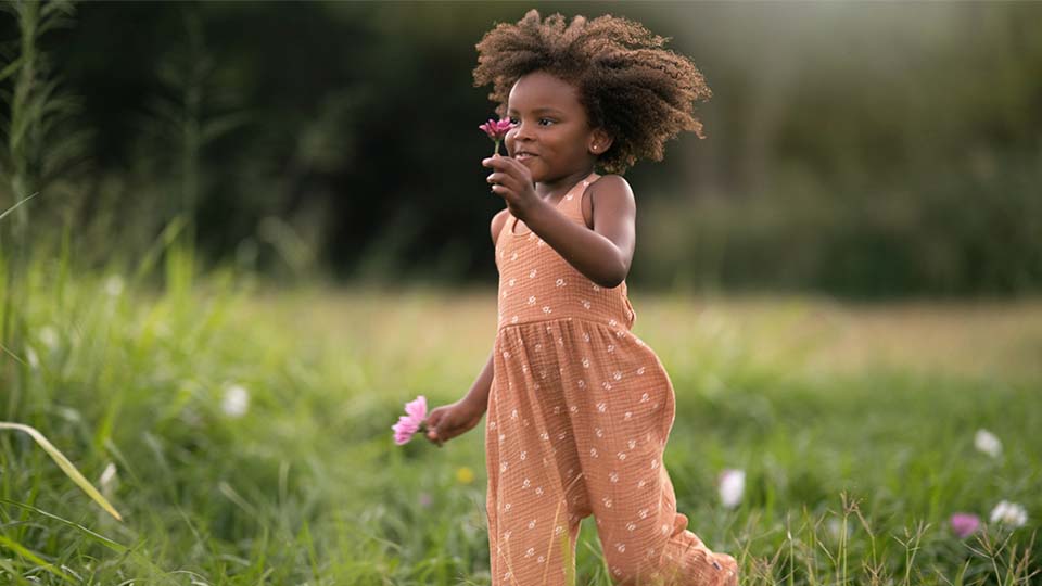 Toddler girl wearing an orange romper running through a field.