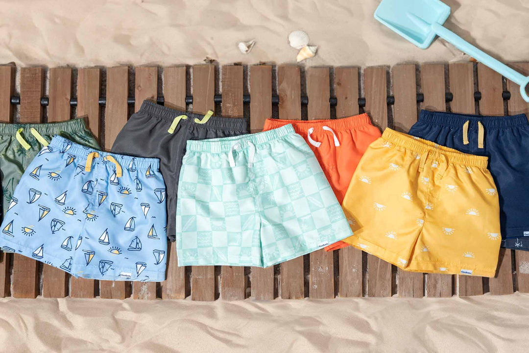 A group of Gerber® Childrenswear swim trunks on a wooden bench.