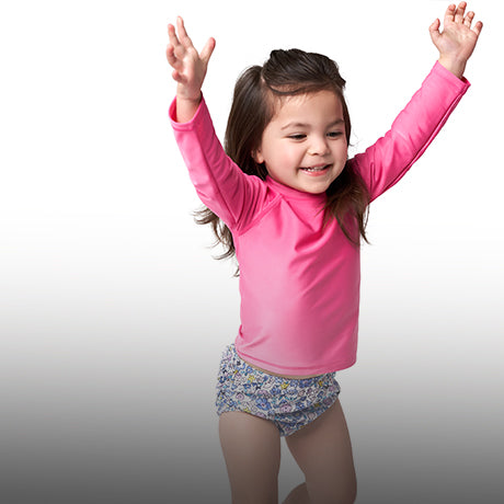 A happy little girl dressed in a pink swimsuit, gleefully jumping up and down.