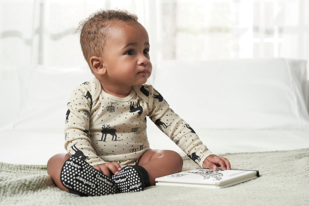 An adorable baby calmly positioned on a bed, captivated by a book, showcasing the beginnings of a love for literature.