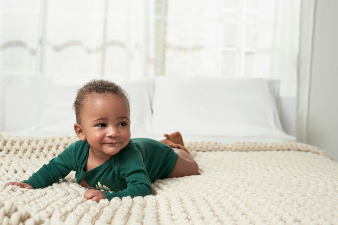 Baby boy with green outfit laying on cable knit blanket.