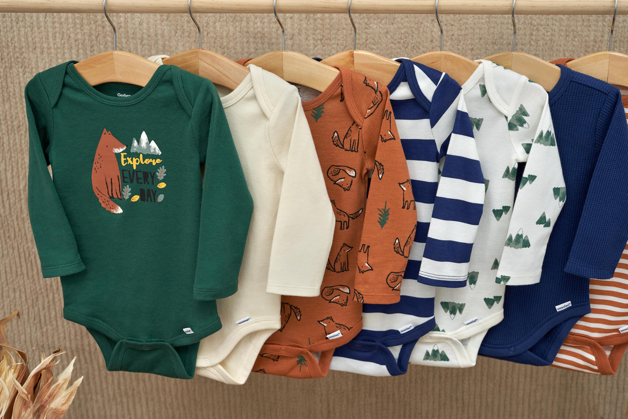 Autumn long sleeve baby onesies hanging on a wooden rod.