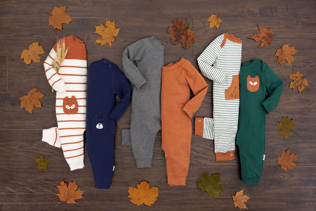 Brown leaves surrounding six autumn baby rompers.