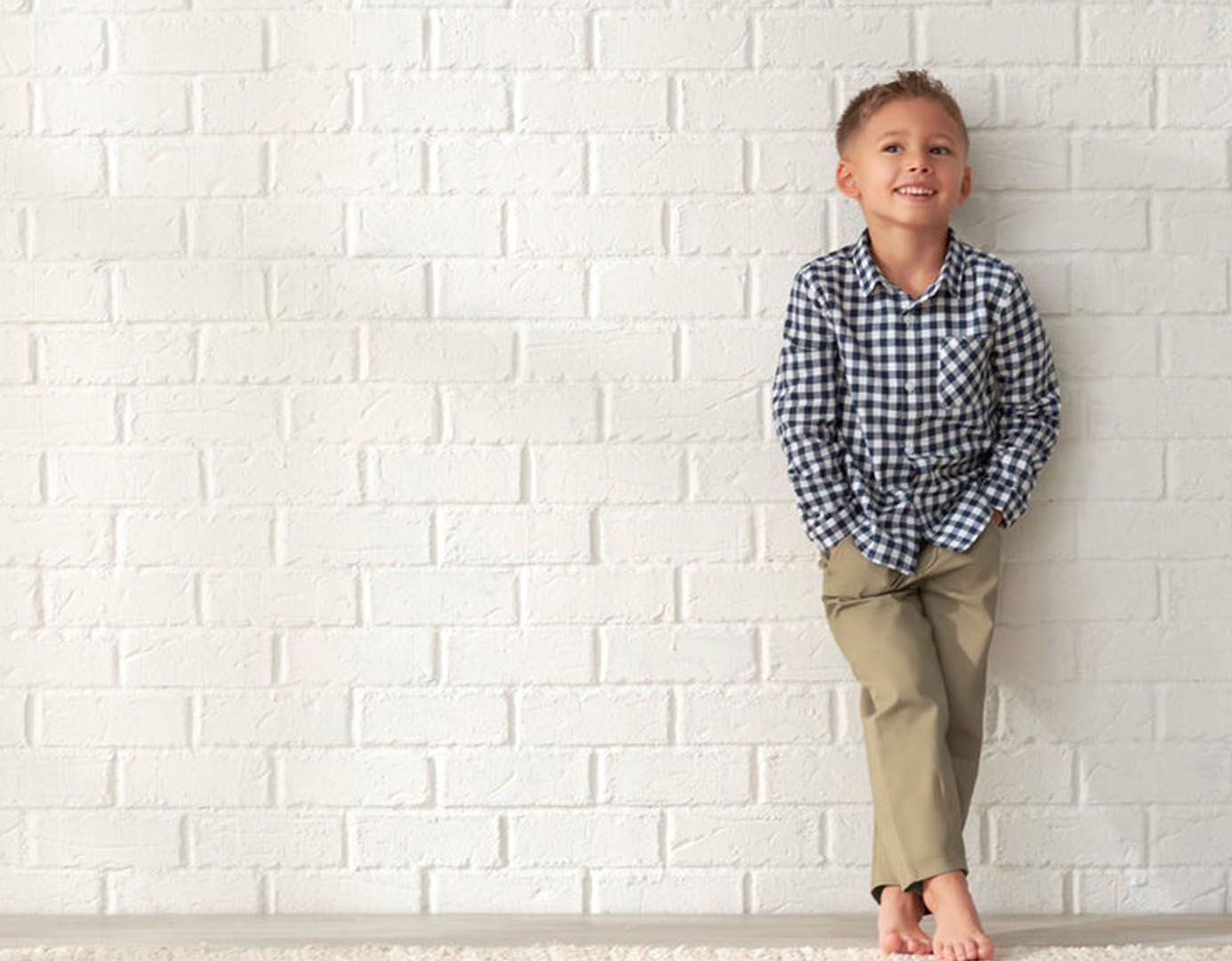 An adorable little boy posing confidently in front of a plain white wall.