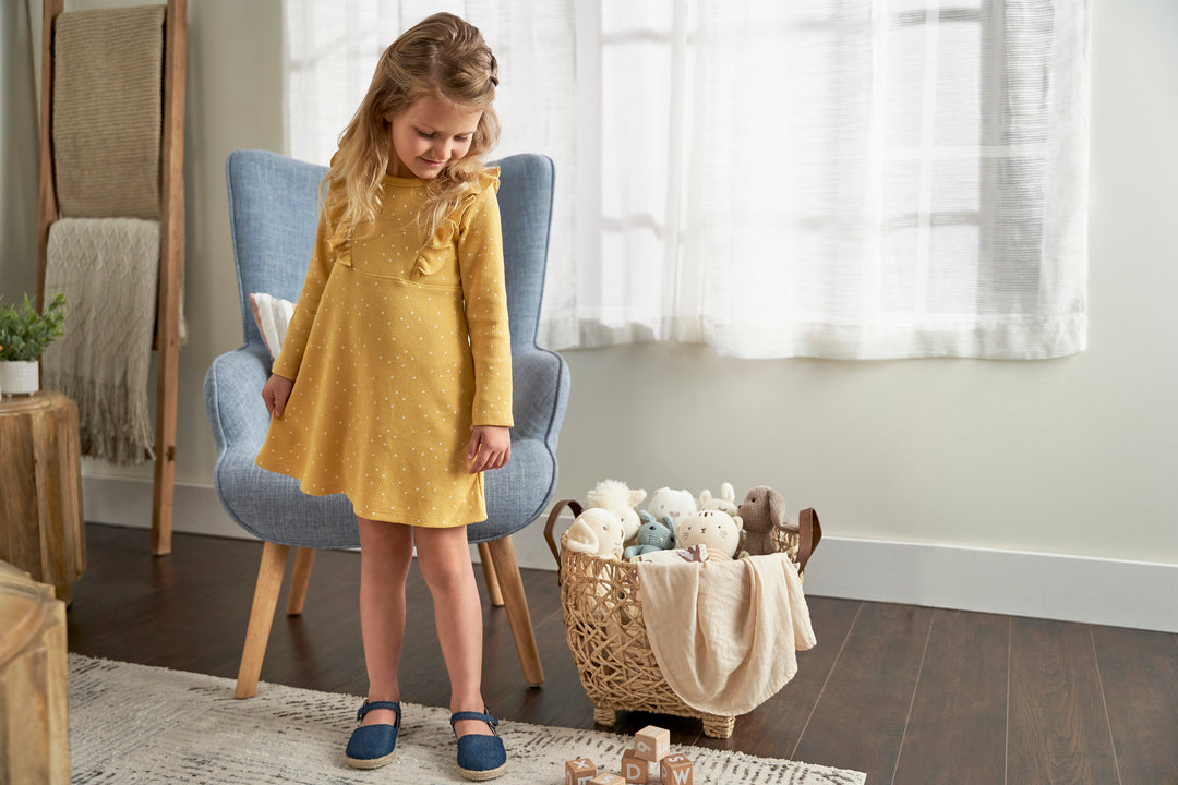 LIttle toddler girl in yellow fall dress looking at toys on the floor.