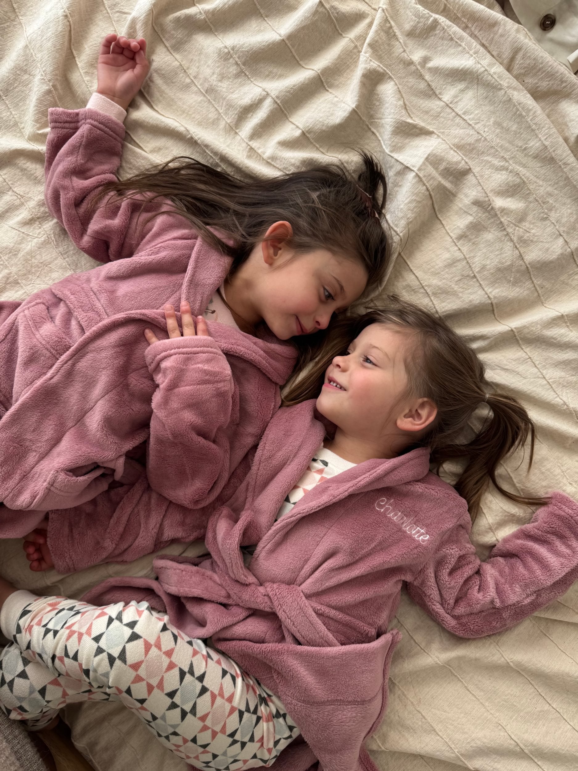 Two children in pink robes lying on a bed