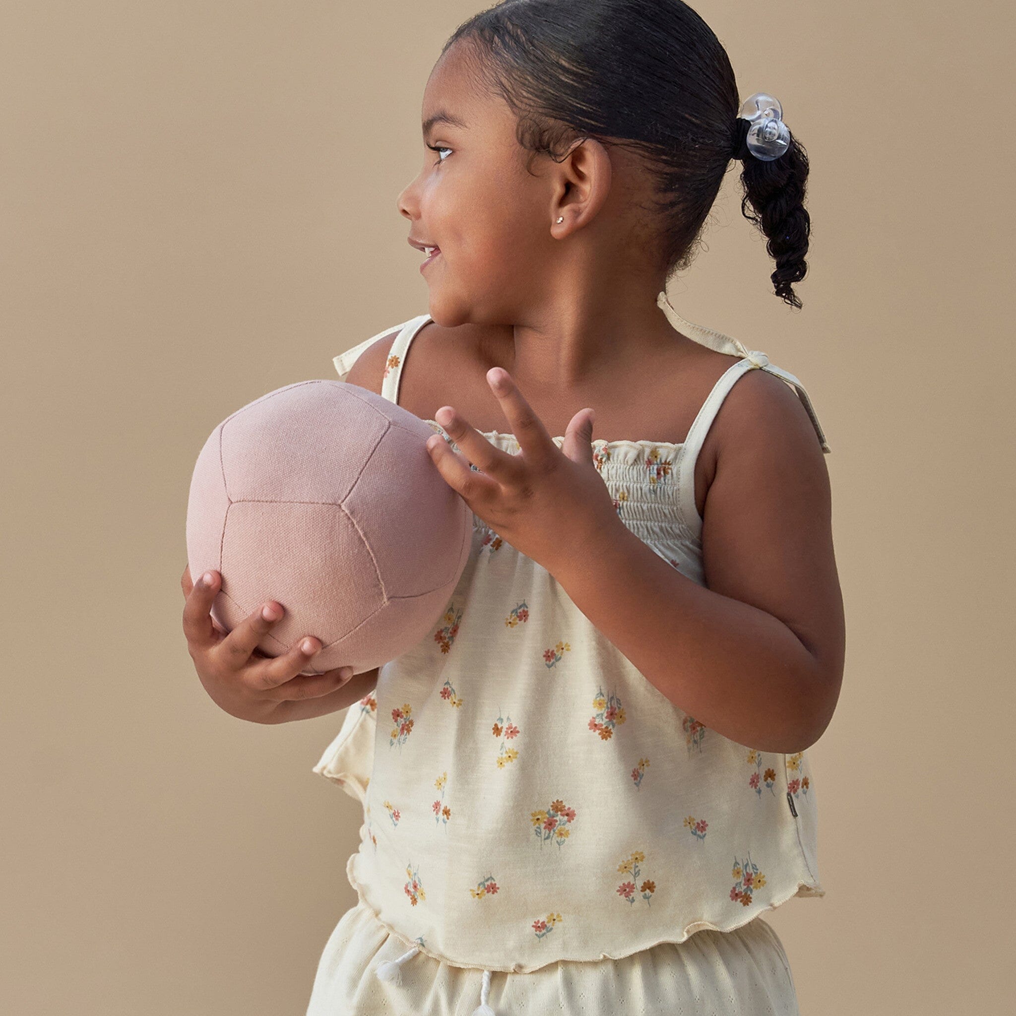Young girl holding a pink ball against a beige background