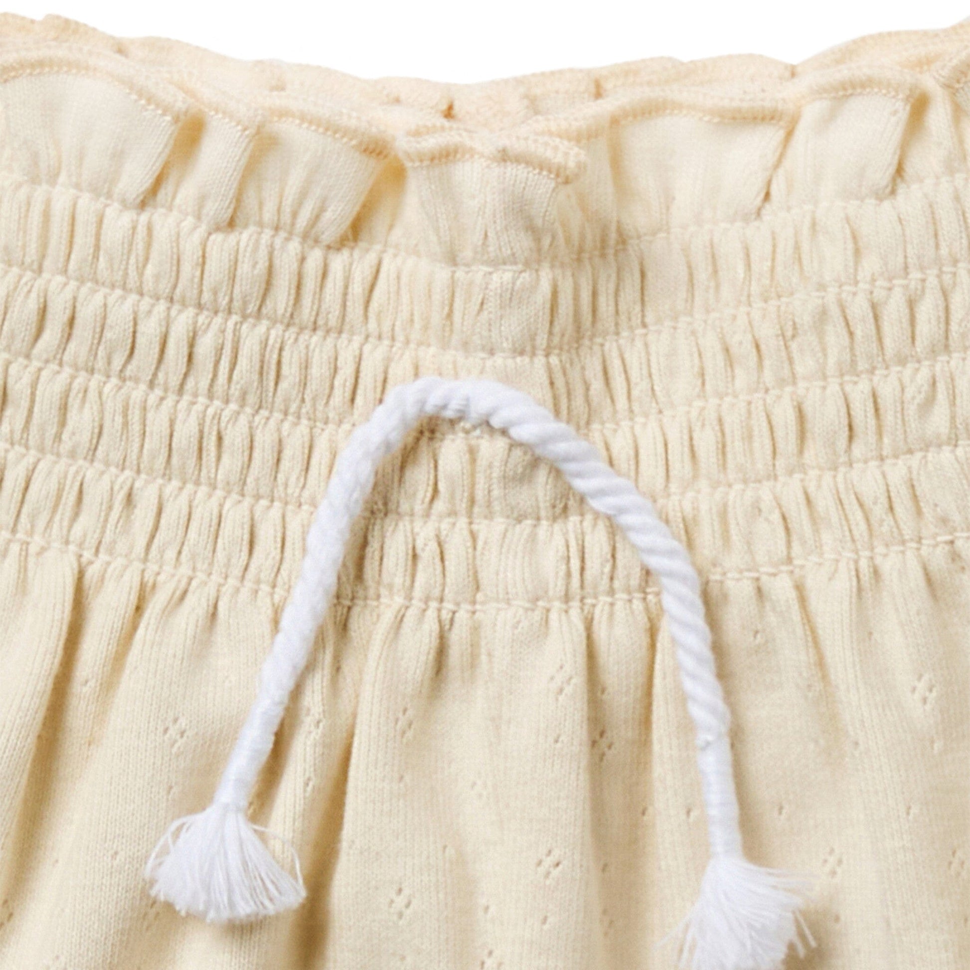 Close-up of beige fabric with a white tassel on a beige background
