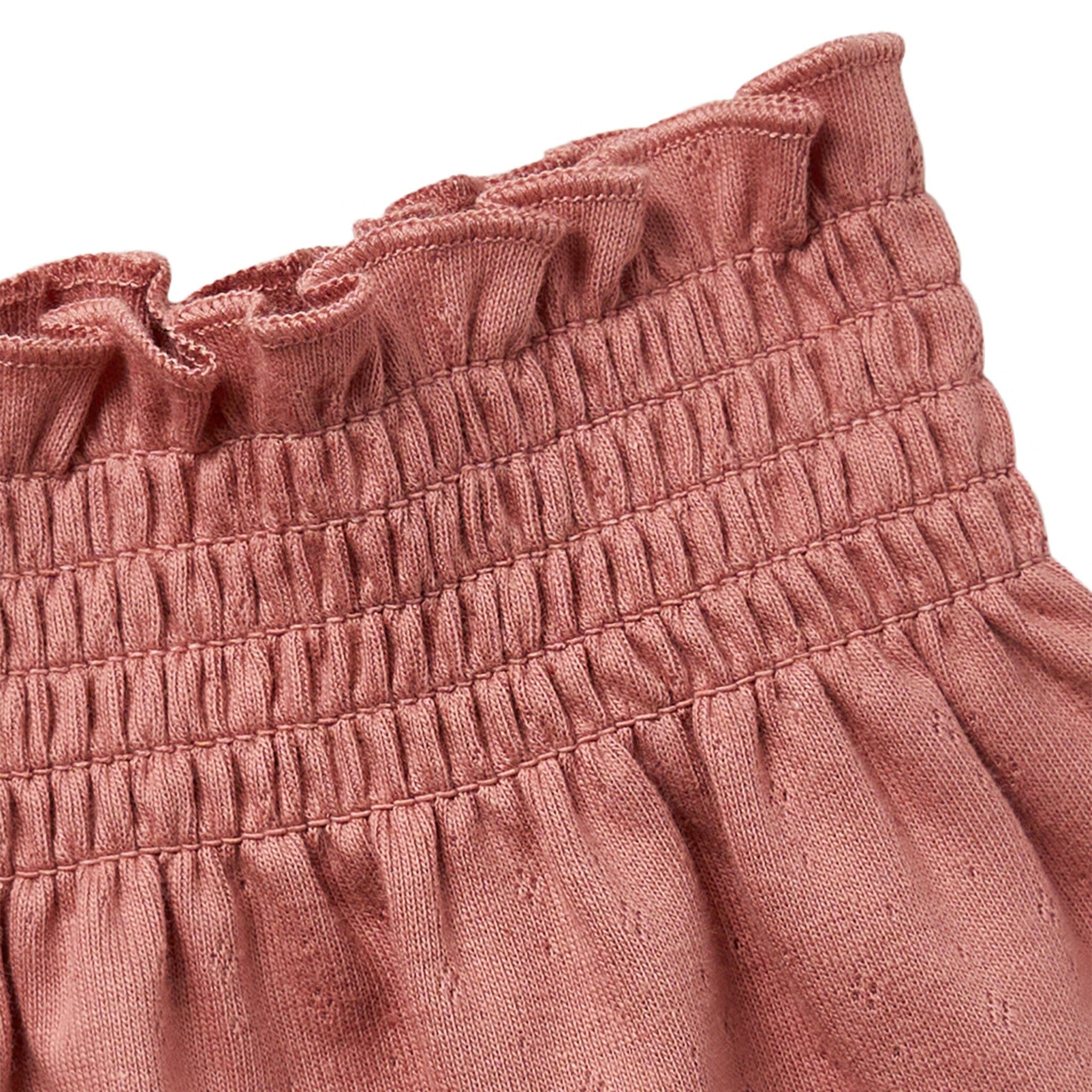 Close-up of a pink textured fabric with ruffled top edge on a white background