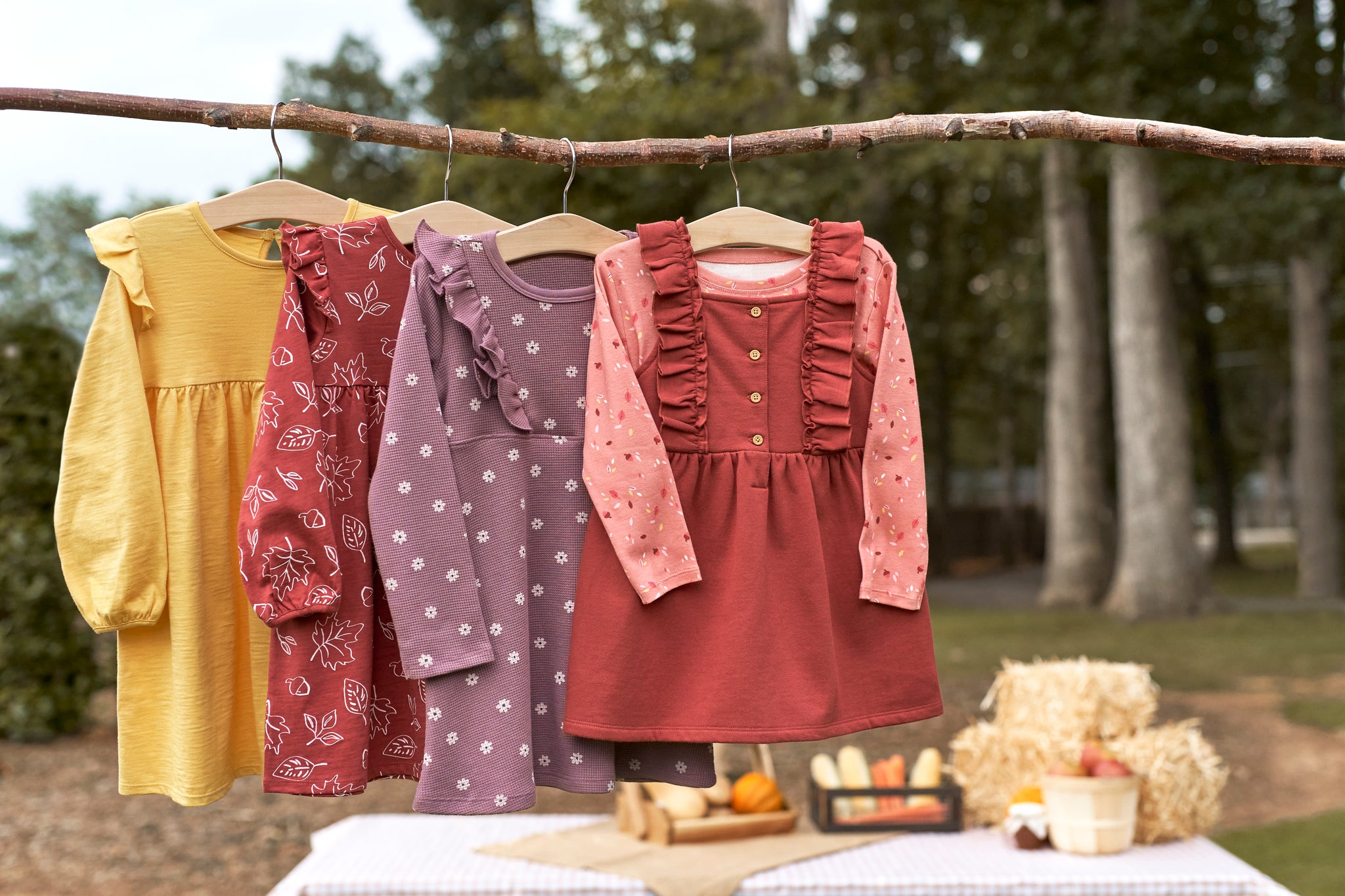 Fall toddler and baby dresses hanging in the woods with hay bales behind them.