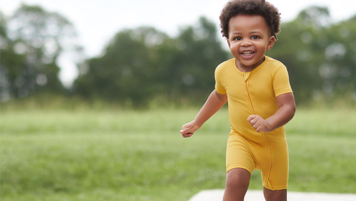 Baby boy in soft zippered bodysuit running and playing outside.